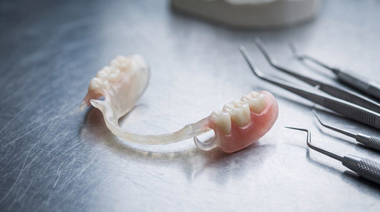 A partial denture built on a slim rigid PEEK framework resting on a dental laboratory bench beside precision instruments